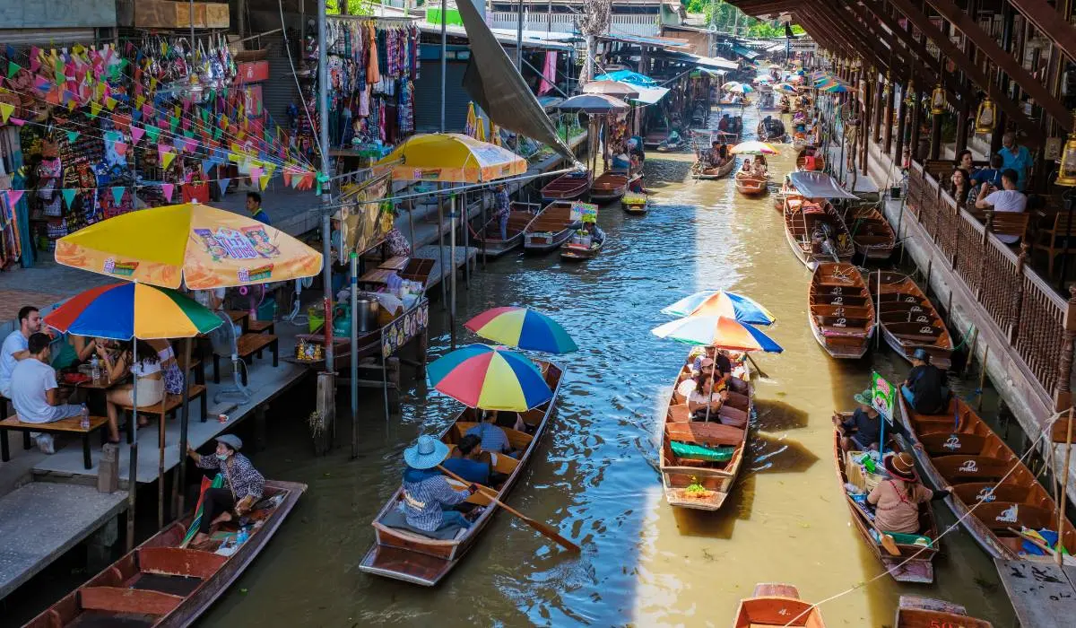 A view of the bustling Damnoen Saduak floating market in Thailand, with vendors selling food and goods from boats on the canal.