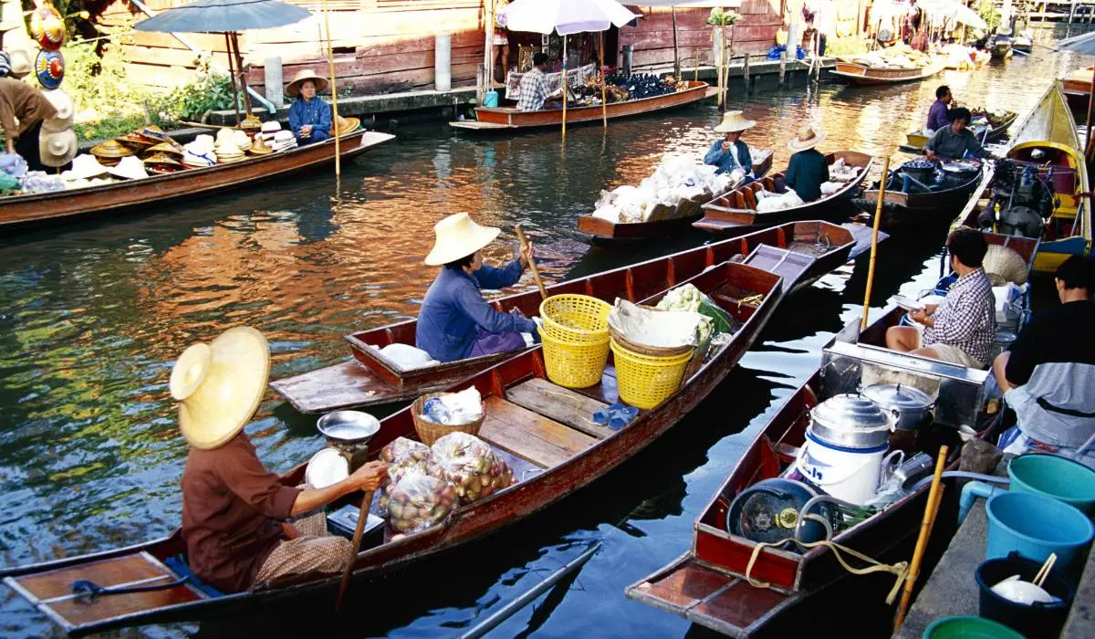 Vibrant floating market scene with vendors in traditional hats paddling wooden boats along a river, selling goods from colorful baskets and metal containers to customers in other boats, reflecting a bustling and cultural exchange on water.