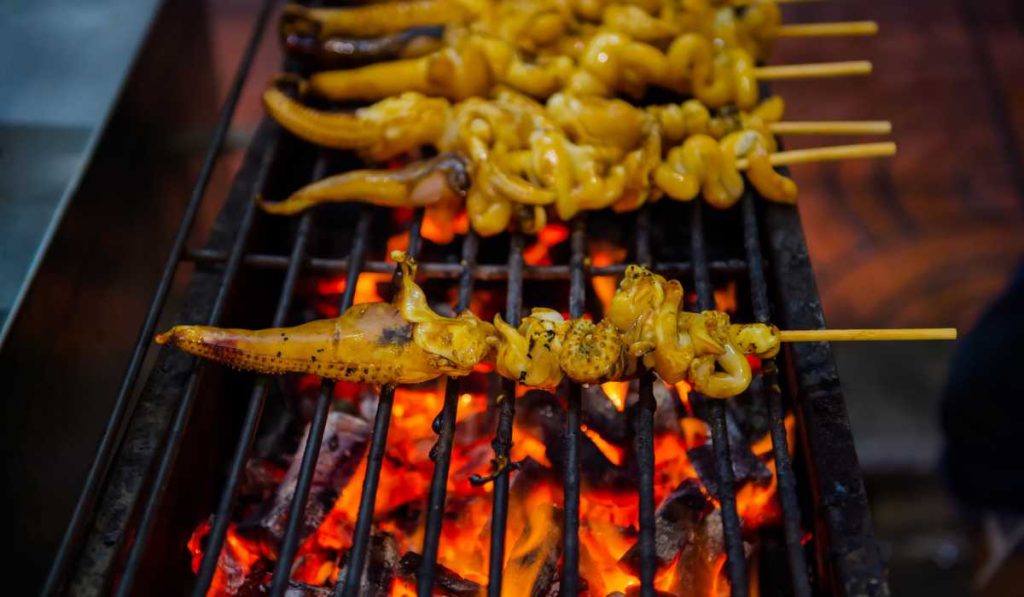 Sizzling skewers of squid grilling over an open flame, with the tentacles and bodies turning a golden brown, capturing the essence of Bangkok's street food scene.
